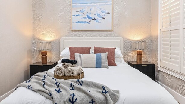 Um quarto com uma cama grande, duas mesas de cabeceira, um quadro na parede e uma janela com persianas.