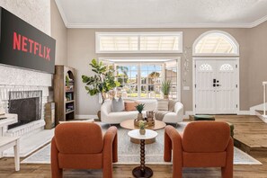 A living room with a fireplace, a couch, two armchairs, a coffee table, and a bookshelf. - 1 Step to the Park - 6BR • Game On! Arcade • BBQ • Pool Table - Long Stay Luxury (Huntington Beach)