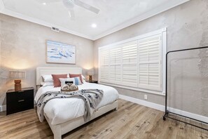 A bedroom with a bed, bedside tables, a ceiling fan, a window with shutters, and a wall-mounted artwork. - 1 Step to the Park - 6BR • Game On! Arcade • BBQ • Pool Table - Long Stay Luxury (Huntington Beach)