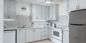 A modern kitchen with white cabinetry, a built-in microwave, a stove, and a refrigerator. - 3BR Holetown Near to Beach, Mango Court - by ZenBreak (Porters)