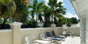 Een zonnig buitenterrein met lounge fauteuils en een tafel, omringd door palmbomen en een witte muur.