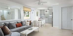 A modern living room with a grey sofa, white dining table, and a kitchen in the background. - 3BR Holetown Near to Beach, Mango Court - by ZenBreak (Porters)