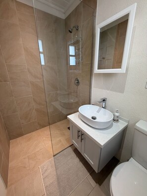 Een badkamer met een douche met glazen wand, een witte wastafel met zeepdispenser en een toilet.