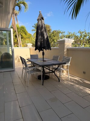 A patio with a table and chairs, an umbrella, and a glass door. - Mango Court #3 - by ZenBreak (Porters)
