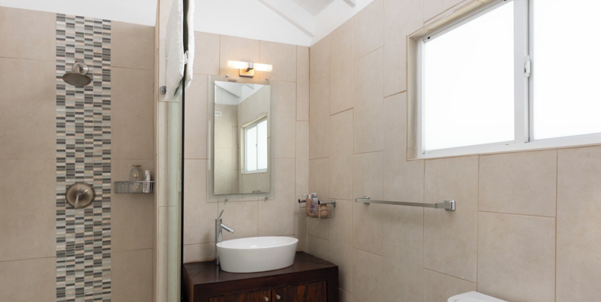 Een badkamer met een douche, een wastafel, een spiegel en een raam.