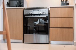 A modern kitchen with a stainless steel oven, wooden cabinets, and a glass door. - StayShort - Peaceful 1-Bedroom, in Dubai Creek Harbour - Sleeps 4 (Dubai Creek Harbour)