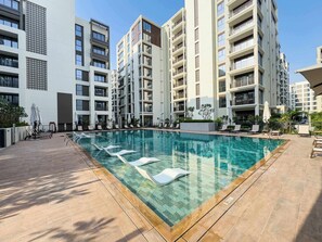 A modern residential building with a swimming pool, sun loungers, and a clear sky. - StayShort - Peaceful 1-Bedroom, in Dubai Creek Harbour - Sleeps 4 (Dubai Creek Harbour)