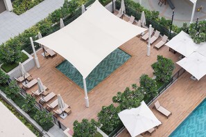 An outdoor pool area with lounge chairs and umbrellas, surrounded by greenery. - StayShort - Peaceful 1-Bedroom, in Dubai Creek Harbour - Sleeps 4 (Dubai Creek Harbour)
