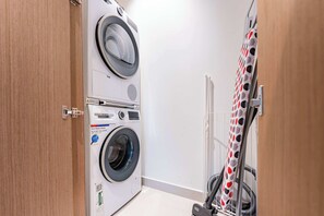 A laundry room with two stacked washing machines, a drying rack, and a caution sign on the door. - StayShort - Peaceful 1-Bedroom, in Dubai Creek Harbour - Sleeps 4 (Dubai Creek Harbour)