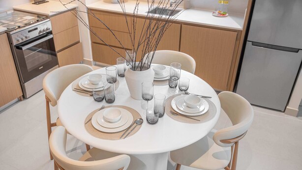 Una cucina moderna con un tavolo da pranzo rotondo apparecchiato per quattro persone, con sedie bianche, bicchieri trasparenti e un vaso con rami.