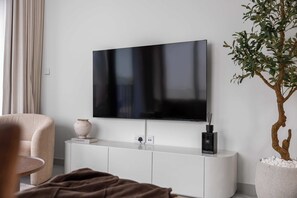 Moderni olohuone, jossa on seinälle asennettu litteänäyttöinen televisio, joka on kiinnitetty valkoiseen tv-tasoon. Huoneessa on myös ruukussa oleva viherkasvi ja beigenvärinen nojatuoli.