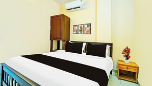 Ein Hotelzimmer mit einem Bett, einem Nachttisch, einem Holzschrank, einer Klimaanlage und drei gerahmten Bildern an der Wand.