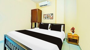 Ein Hotelzimmer mit einem Bett, einem Nachttisch, einem Holzkoffer, einer Klimaanlage und einem an der Wand hängenden Bild.