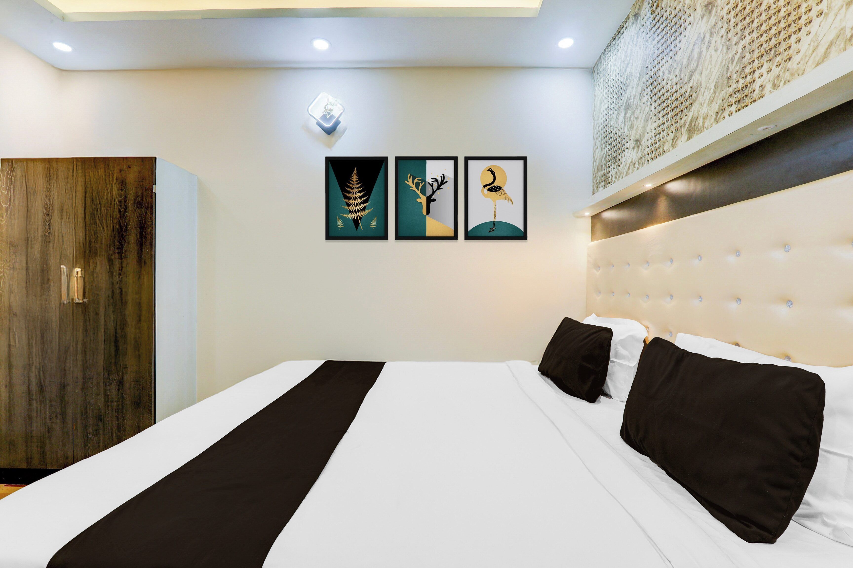 A hotel room with a bed, a wardrobe, and three framed artworks on the wall.