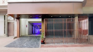 Una entrada de edificio con un portón metálico, suelo de baldosas y un pasillo que conduce a un interior bien iluminado.