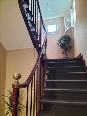 A staircase with a wooden handrail and balusters, leading to a landing with a potted plant. - Apartment 50 meters from the ocean, with the train station and shops nearby (Houlgate)
