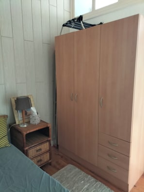 A bedroom with a wooden wardrobe, a bedside table with a lamp, and a bed. - Apartment 50 meters from the ocean, with the train station and shops nearby (Houlgate)