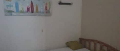 A single bed with a wooden frame and two pillows, a small painting on the wall, and a simple nightstand.