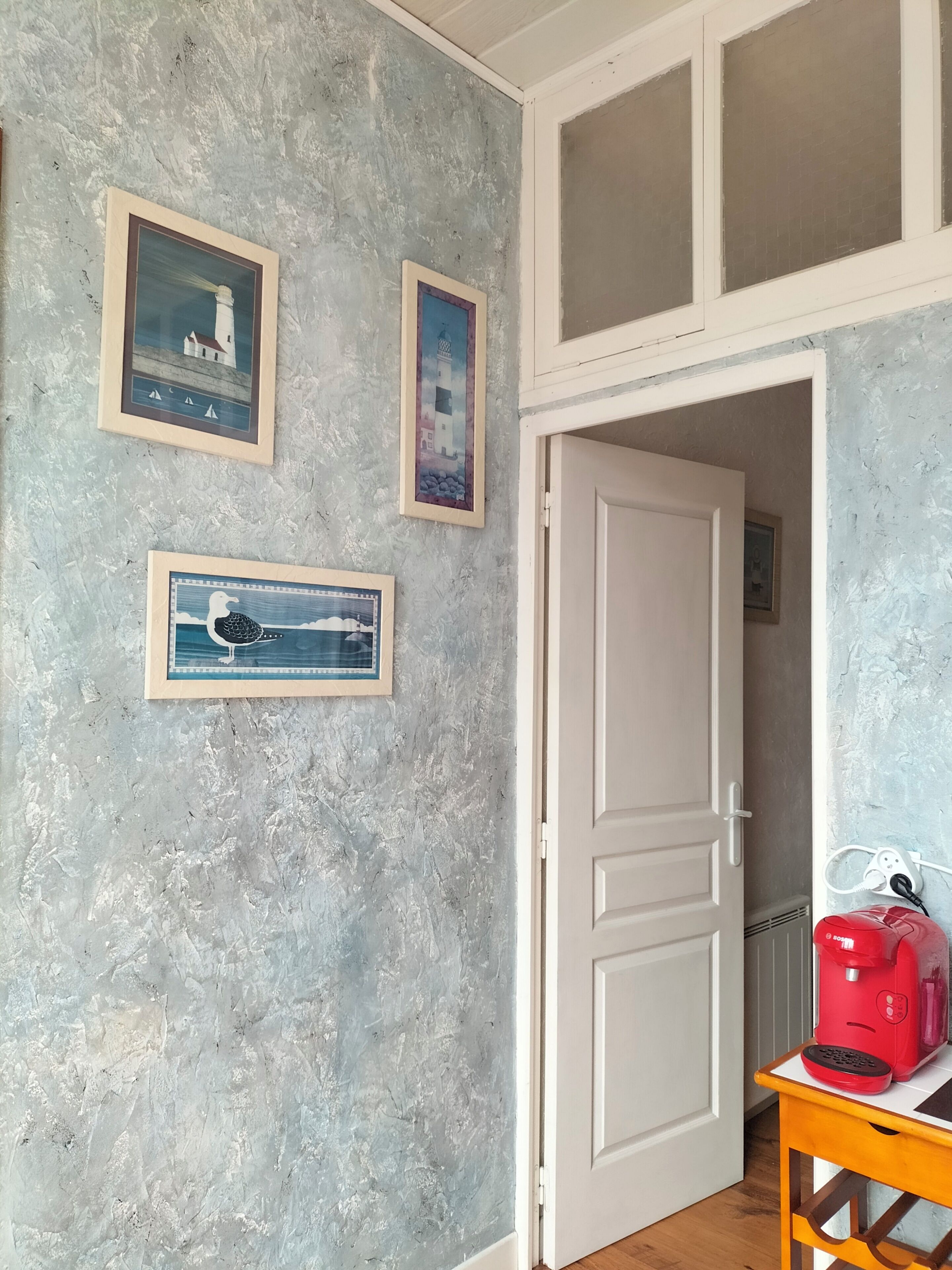 A room with a textured wall, a white door, and a small table with a red object on it.