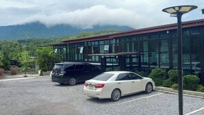 A parking area with two cars, a building with large windows, and a mountainous backdrop.