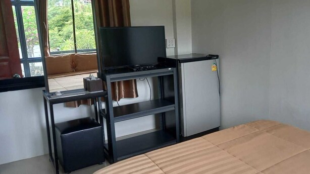 A room with a bed, a television on a stand, a refrigerator, and a window with curtains. - Lilly Home (Khaem Son)