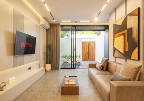 Ein modernes Wohnzimmer mit Flachbildfernseher, einer Couch, einem Couchtisch und einer Glastür, die zu einem Außenbereich führt.