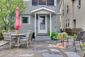 A patio with a table and chairs, a potted plant, and a door with a small porch. - Walk to Main St Stroudsburg! Historic Dtwn Home (Stroudsburg)