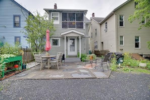 A two-story house with a patio area featuring a table and chairs, surrounded by a garden with various plants and flowers. - Walk to Main St Stroudsburg! Historic Dtwn Home (Stroudsburg)