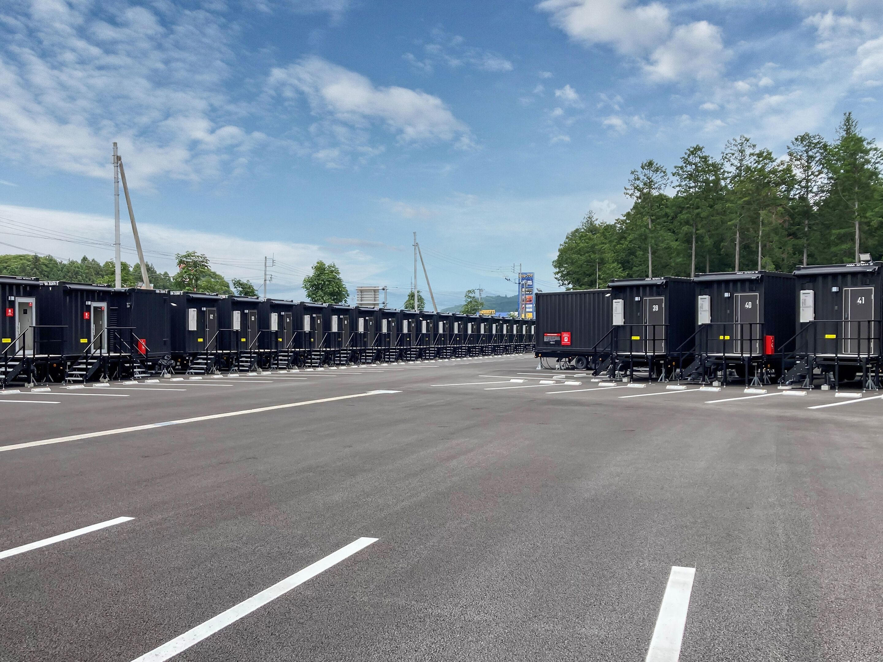 A parking lot with rows of black train carriages, white parking lines, and a clear sky.