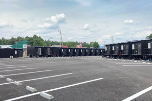 A parking lot with multiple black containers, some with doors and windows, and a building with a green roof in the background.