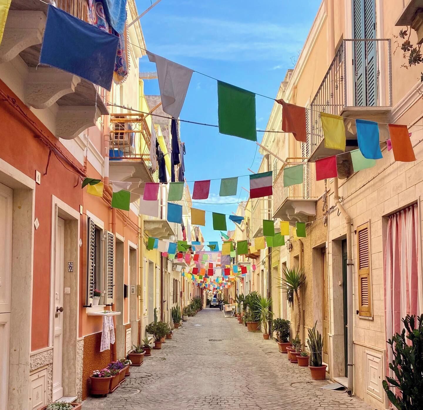 Una calle estrecha bordeada de edificios, algunos con balcones, y banderas de colores colgadas.