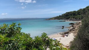 A coastal beach with clear turquoise waters, rocky shoreline, and dense greenery. - Maison Tabarka: Comfort and Design Suites in the Historic Center of Carloforte (Carloforte)