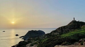 A coastal landscape with a lighthouse on a hill, a clear sky, and calm sea. - Maison Tabarka: Comfort and Design Suites in the Historic Center of Carloforte (Carloforte)