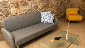 A grey sofa with a patterned pillow, a yellow armchair, and a glass coffee table with a tennis racket. - Maison Tabarka: Comfort and Design Suites in the Historic Center of Carloforte (Carloforte)