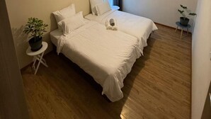 Quarto com duas camas, uma planta em vaso, uma mesinha e uma luminária no teto.