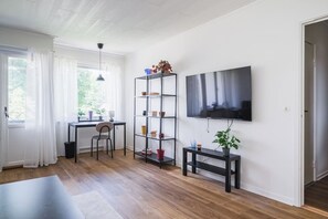 Una sala de estar moderna con una televisión de pantalla plana, un escritorio con una silla, una estantería y una planta en maceta.