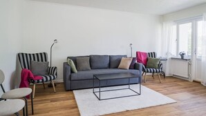 A living room with a grey sofa, striped chairs, a white rug, and a window with curtains.