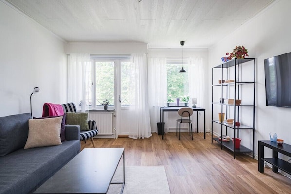 A modern living room with a sofa, a dining table, and a TV mounted on the wall.