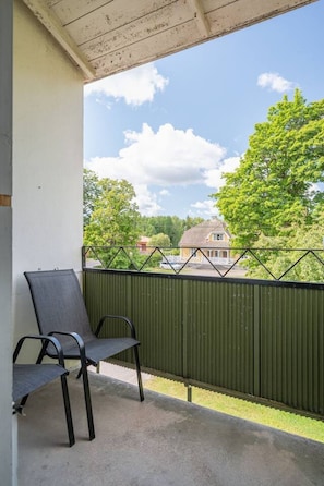 A balcony with a metal railing, two chairs, and a view of a residential area with trees and a house.