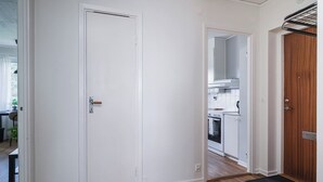 A hallway with a white door, a wooden floor, and a view into a kitchen area.