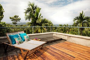 A wooden deck with a lounge chair and cushions, overlooking a lush landscape with palm trees. - Jalakara Havelock (Port Blair)