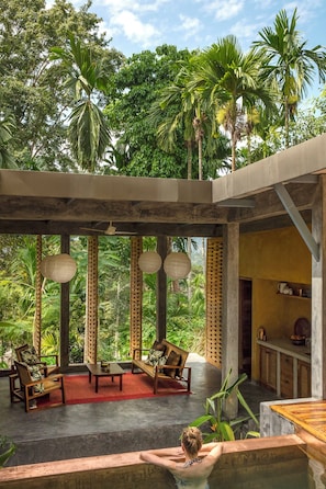 A tropical outdoor seating area with a pool, wooden furniture, and a view of dense foliage. - Jalakara Havelock (Port Blair)