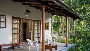 A covered outdoor seating area with wooden furniture, a hammock, and a view of lush greenery.