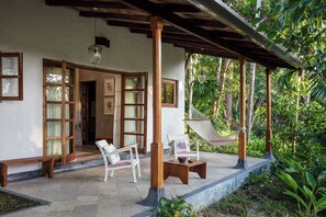 A covered outdoor seating area with wooden furniture, a hammock, and a view of lush greenery. - Jalakara Havelock (Port Blair)