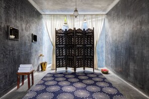 A room with a patterned carpet, a wooden stool with towels, a decorative screen, and a hanging light fixture.