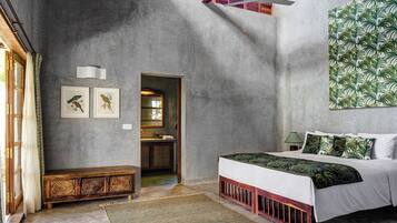 A bedroom with a bed, a bench, a door leading to a bathroom, and a wall with a leaf pattern.