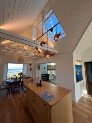 A spacious kitchen with a wooden island, a dining area with wicker chairs, and a view of the ocean through large windows. - New Stunning house St Ives with parking (Saint Ives)