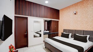 Ein Hotelzimmer mit einem großen Bett, einem Kleiderschrank, einem Spiegel, einem Fernseher und einem kleinen Tisch mit Blumenvase.