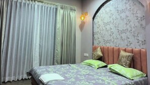 A bedroom with a bed, a ceiling fan, an air conditioning unit, and a window with curtains. - Shourya Resort and lawn Panhala (Panhala)