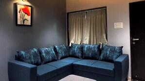 A modern living room with a sectional sofa, a small coffee table, a ceiling fan, and a painting on the wall. - Shourya Resort and lawn Panhala (Panhala)